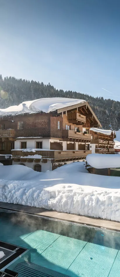 Wellness hotel with heated outdoor pool in snowy alpine landscape under sunny blue sky
