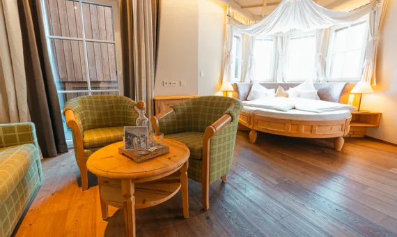 Cozy hotel room with round wooden bed, green armchairs, and natural lighting