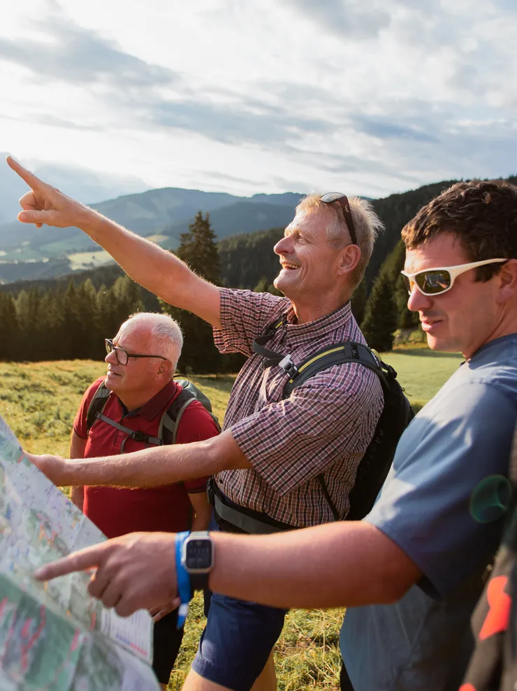 Wandergruppe liest Karte und zeigt auf Berge in alpiner Landschaft