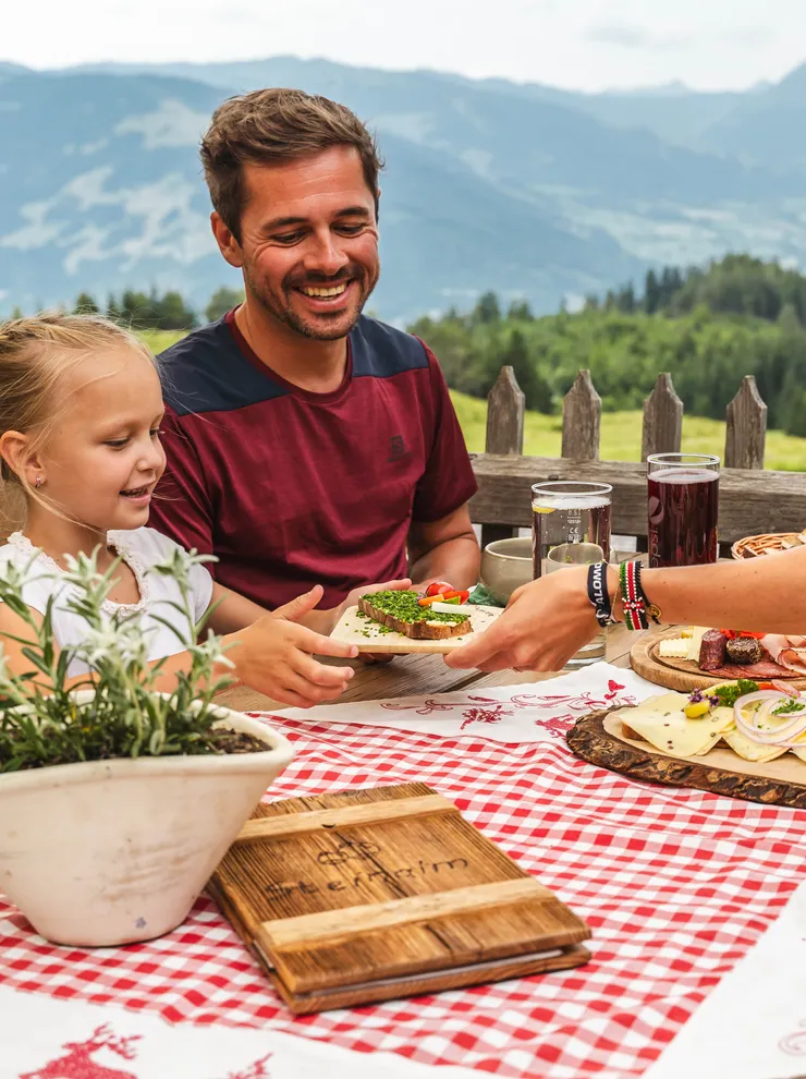 Family enjoying traditional alpine lunch on wooden terrace with mountain view