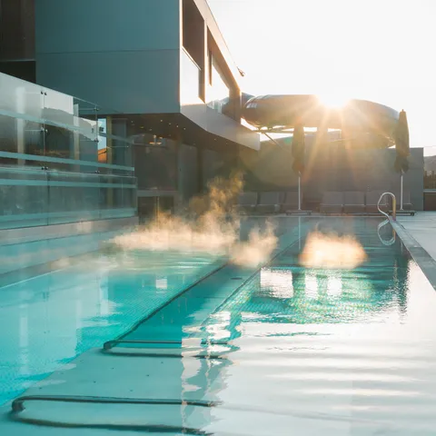 Steam rising from heated outdoor pool at modern hotel during sunrise