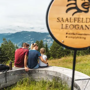 Family sitting on wooden bench overlooking mountains in Saalfelden Leogang during hike