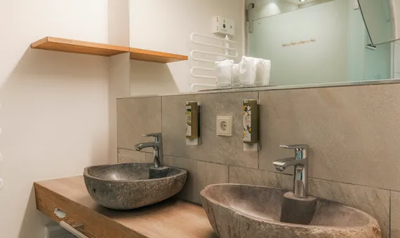 Modern hotel bathroom with stone vessel sinks on wooden counter and wall-mounted soap dispensers