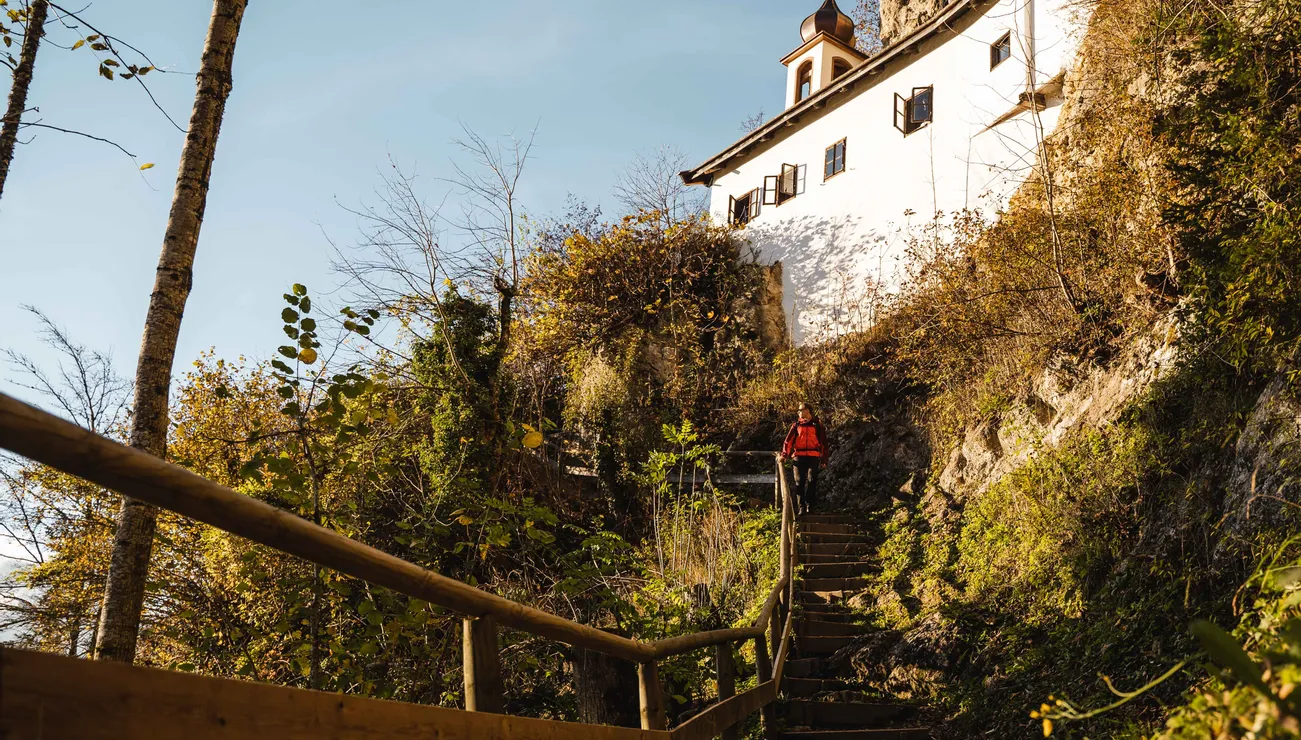 Wanderer steigt Holztreppe durch Herbstwald zu einem Kloster am Felsen hinauf