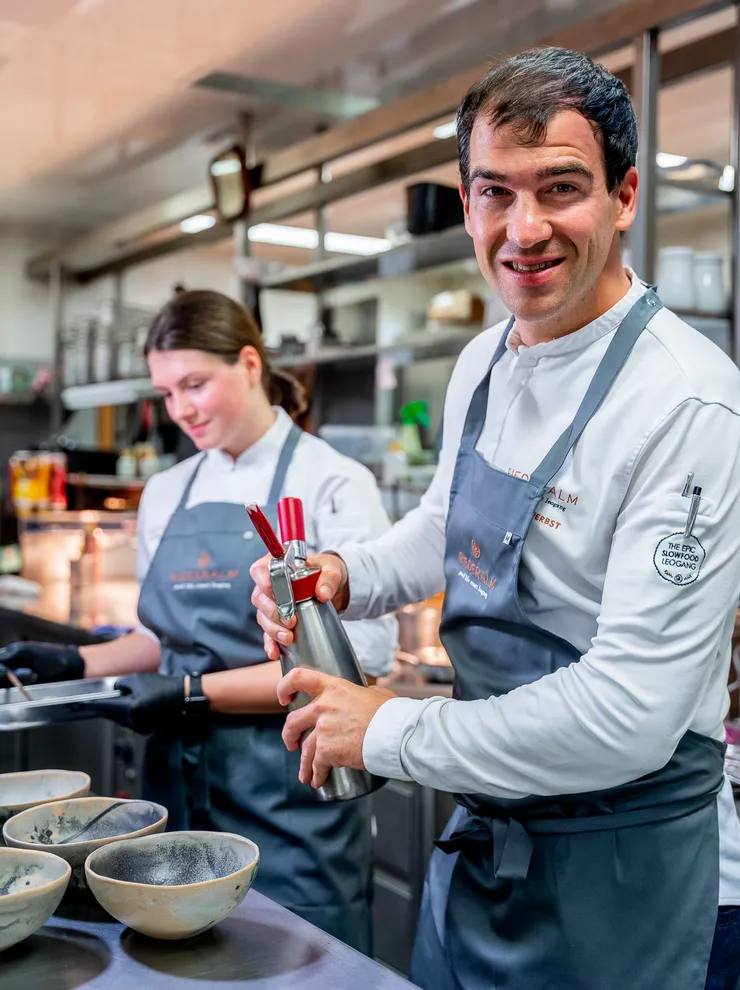 Smiling chef using a cream whipper in a professional kitchen with ceramic bowls in front