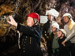Tour guide with red helmet explaining rock formations to family inside a cave
