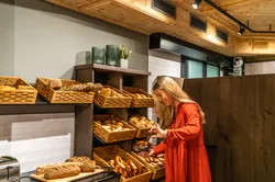 Frau wählt Brezeln aus einem Holzregal mit Brot in einer gemütlichen Bäckerei
