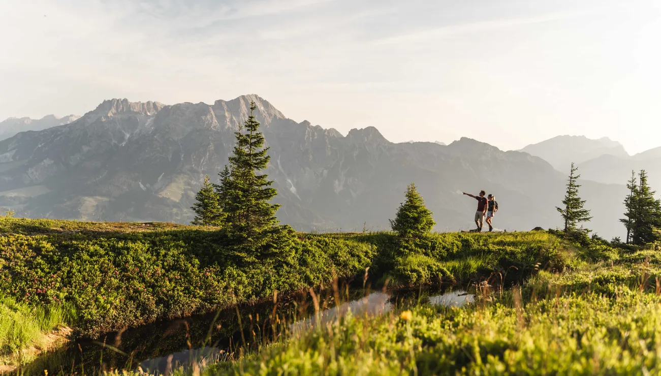 Wanderer auf einem alpinen Pfad mit Blick auf ein Bergpanorama bei Sonnenuntergang