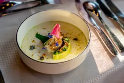 Gourmet soup with cream, avocado, edible flowers and herbs in a white bowl