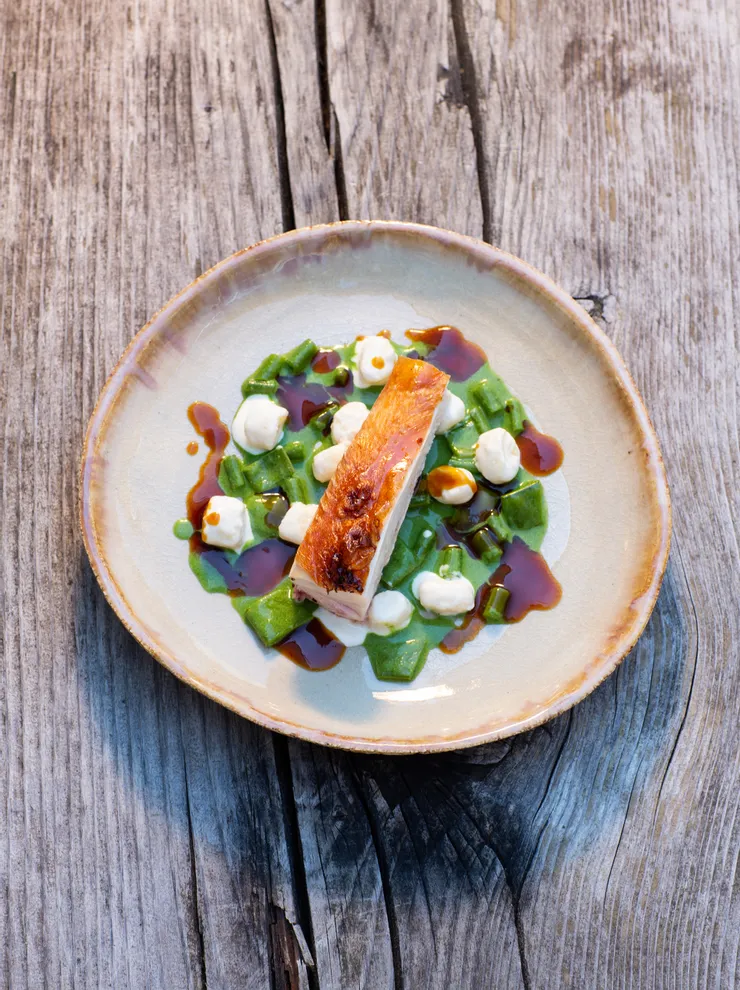 Gourmet roasted chicken breast served with green pasta, sauce drops and cream on rustic plate