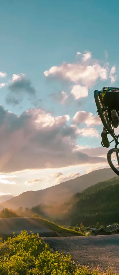 Mountain biker performing a jump at sunset with scenic alpine landscape in background