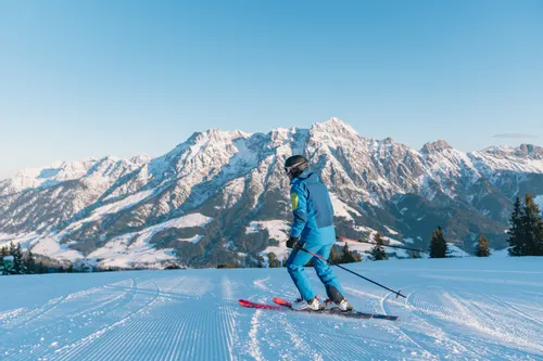 Skier on groomed slope with snow-covered alpine mountains in the background
