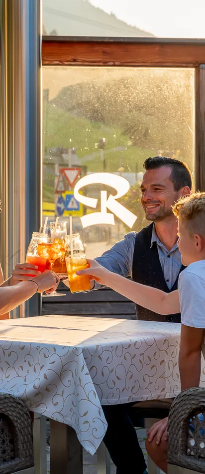 Familie stößt mit Getränken auf einer sonnigen Restaurantterrasse in den Bergen an