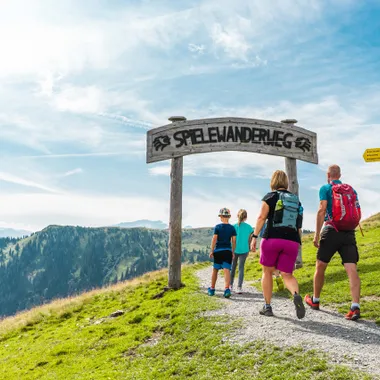 Family hiking on the Spielewanderweg trail in the Alps under sunny skies