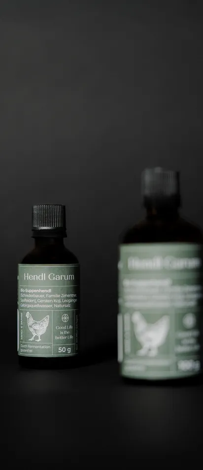 Zwei Flaschen Hendl Garum Bio-Suppenwürze mit grünem Etikett auf schwarzem Hintergrund
