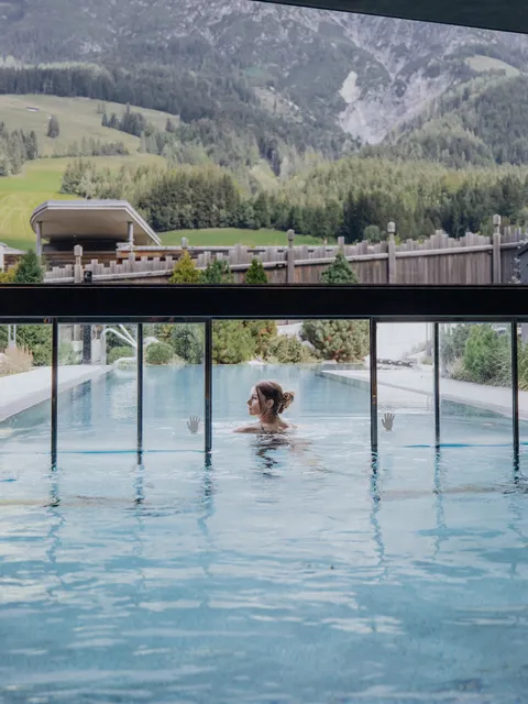 Woman relaxing in an outdoor heated pool with mountain view in luxury spa resort