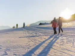 People walking and skiing on snowy slope at sunset in mountain resort
