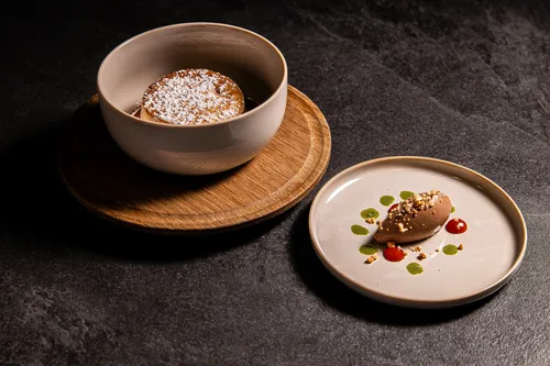 Schokoladensoufflé mit Puderzucker und Mousse mit Soßentropfen auf dunklem Steinuntergrund