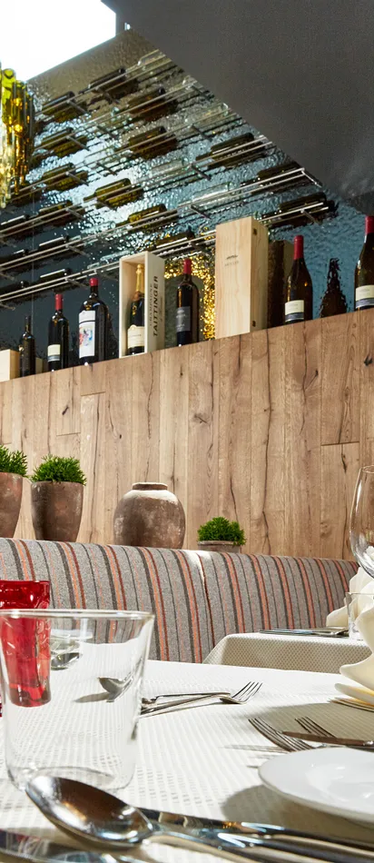 Elegant restaurant interior with set tables, wine glasses, and decorative wine bottle chandelier