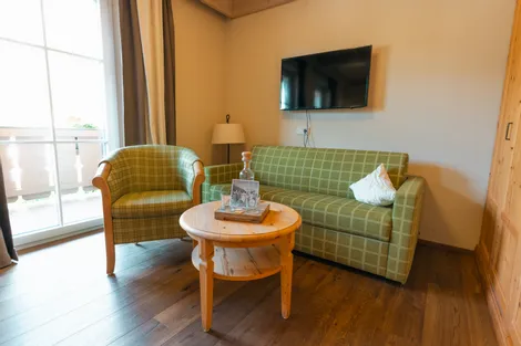 Cozy hotel room with green checkered sofa, armchair, round wooden table and wall-mounted TV