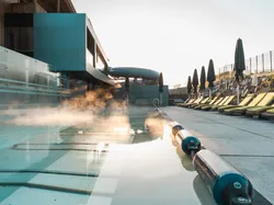 Dampfer auf beheiztem Außenpool neben moderner Hotelterrasse mit Sonnenliegen