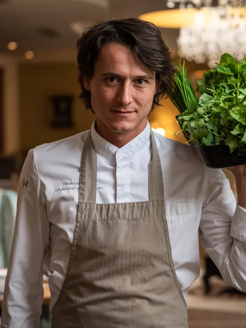 Chef holding a container of fresh herbs in a stylish restaurant setting