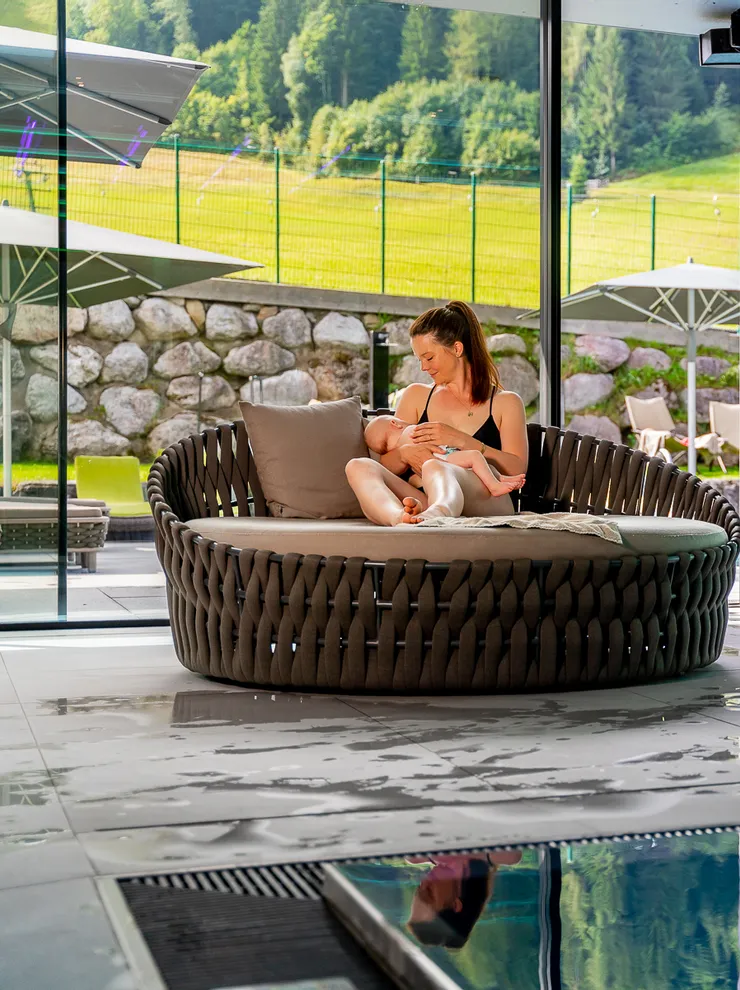 Mother breastfeeding baby by indoor pool with scenic mountain view