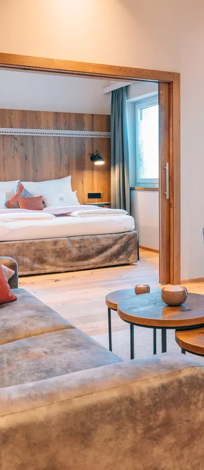 Moderne Hotelsuite mit gemütlicher Sitzecke, runden Tischen und Blick ins Schlafzimmer