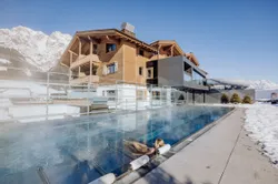 Woman relaxing in heated outdoor pool at alpine resort with snowy mountain view