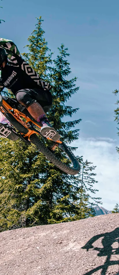 Mountainbiker springt in der Luft von einer Schanze im Waldtrail
