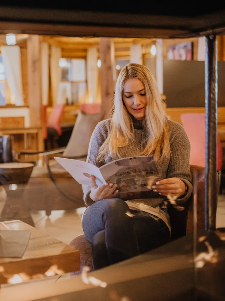 Woman reading a menu in a cozy rustic lounge with warm ambient lighting and fireplace