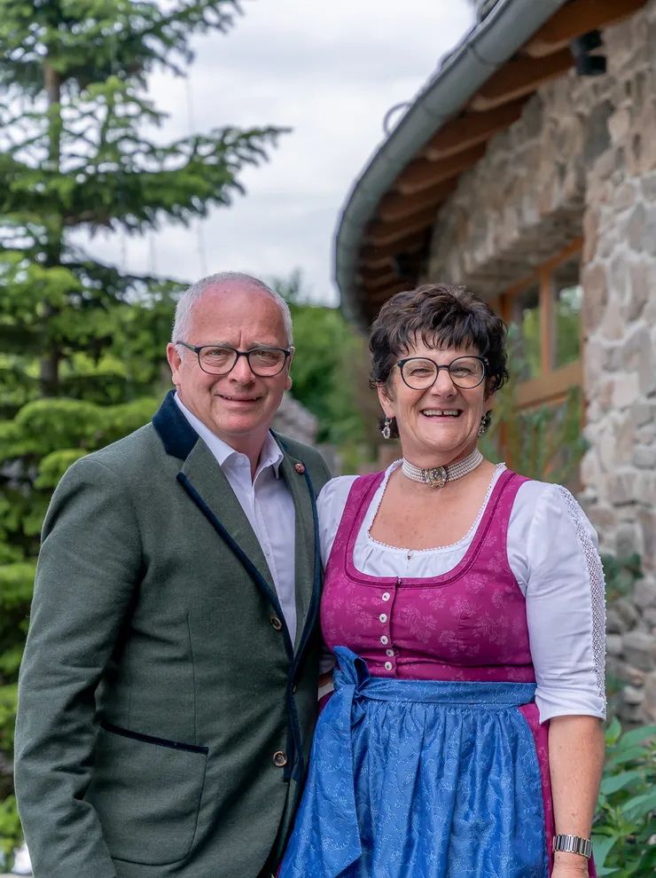 Smiling couple in traditional Bavarian clothing standing outdoors near a stone house