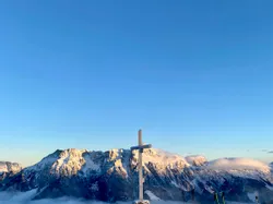 Verschneiter Gipfel mit Gipfelkreuz und Skiern, Blick auf Alpen bei Sonnenaufgang