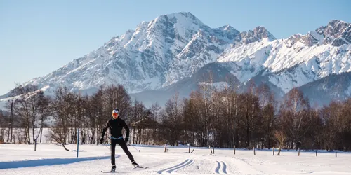 Langläufer gleitet durch verschneite Landschaft mit Alpen im Hintergrund