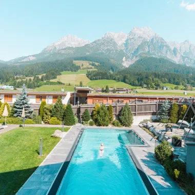 Außenpool mit Liegestühlen vor Alpenkulisse in sonniger Hotelanlage