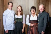 Four people in traditional Austrian clothing and modern chef uniform posing together indoors