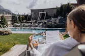Frau liest Wellnessbroschüre im Bademantel am Pool im Spa-Hotel