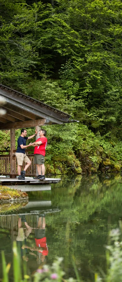Zwei Männer unterhalten sich auf einer Holzterrasse am See im Wald