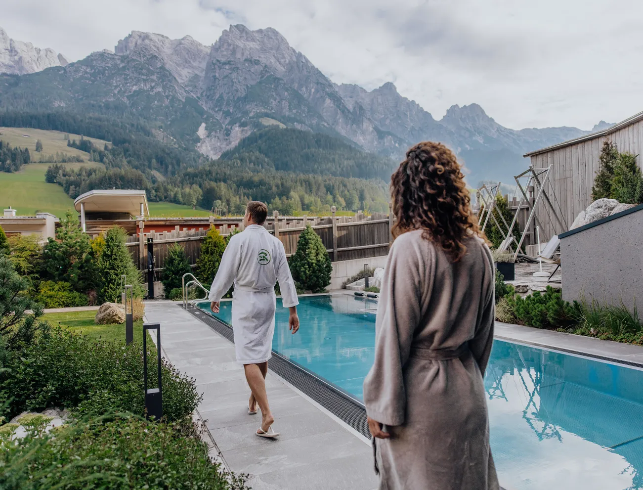 Paar in Bademänteln am Außenpool eines Alpen-Wellnesshotels mit Bergblick