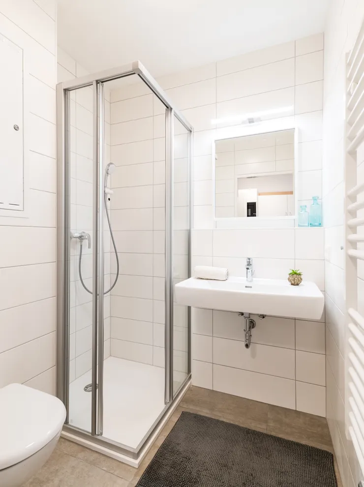 Modern white-tiled bathroom with shower cabin, wall-mounted toilet and sink
