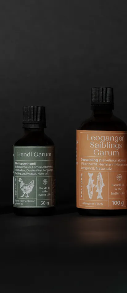 Four bottles of organic chicken and char garum on black background