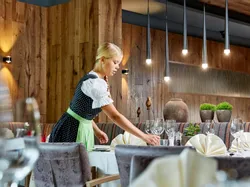 Waitress in traditional dirndl setting table in upscale rustic restaurant