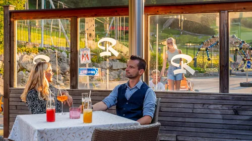 Paar genießt bunte Getränke im Restaurant mit Blick auf Spielplatz bei Sonnenuntergang
