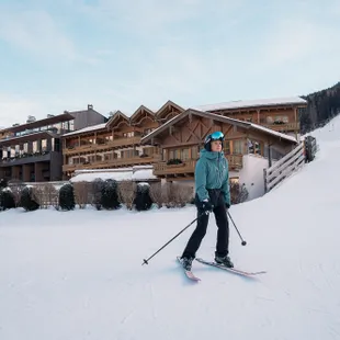 Skifahrer auf verschneiter Piste vor einem alpinen Skigebiet mit Chalets aus Holz