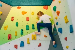 Child climbing indoor bouldering wall with colorful holds shaped like letters