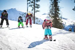 Kinder fahren in einer Reihe einen sonnigen verschneiten Berghang hinunter