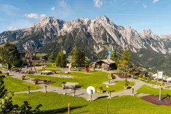 Spielplatz mit Alpenpanorama und Holzhütten bei Sonnenschein