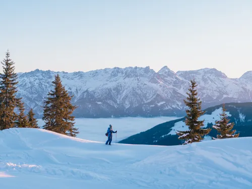 Wanderer mit Skistöcken im verschneiten Gebirge bei Sonnenaufgang