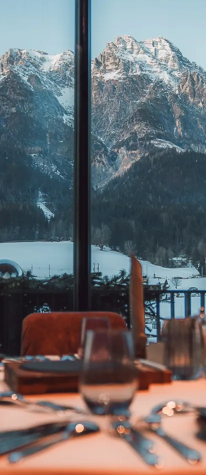 Elegant gedeckter Restauranttisch mit Blick auf schneebedeckte Alpen durch großes Fenster