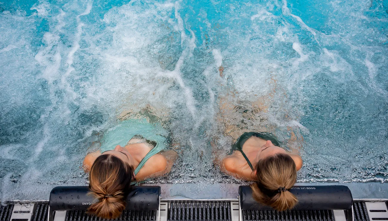 Zwei Frauen entspannen auf Poolliegen im sprudelnden Whirlpool eines Spas